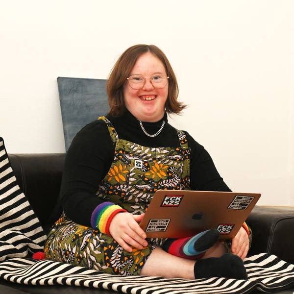 Eine junge Frau sitzt im Schneidersitz auf dem Sofa, auf den Knien hat sie einen Laptop.