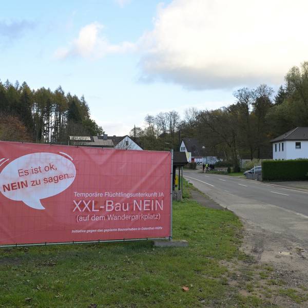 Ein großes, rotes Plakat weist auf Protest gegen den Bau einer Flüchtlingsunterkunft hin.