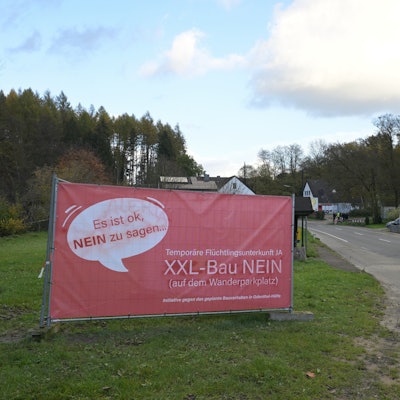 Ein großes, rotes Plakat weist auf Protest gegen den Bau einer Flüchtlingsunterkunft hin.