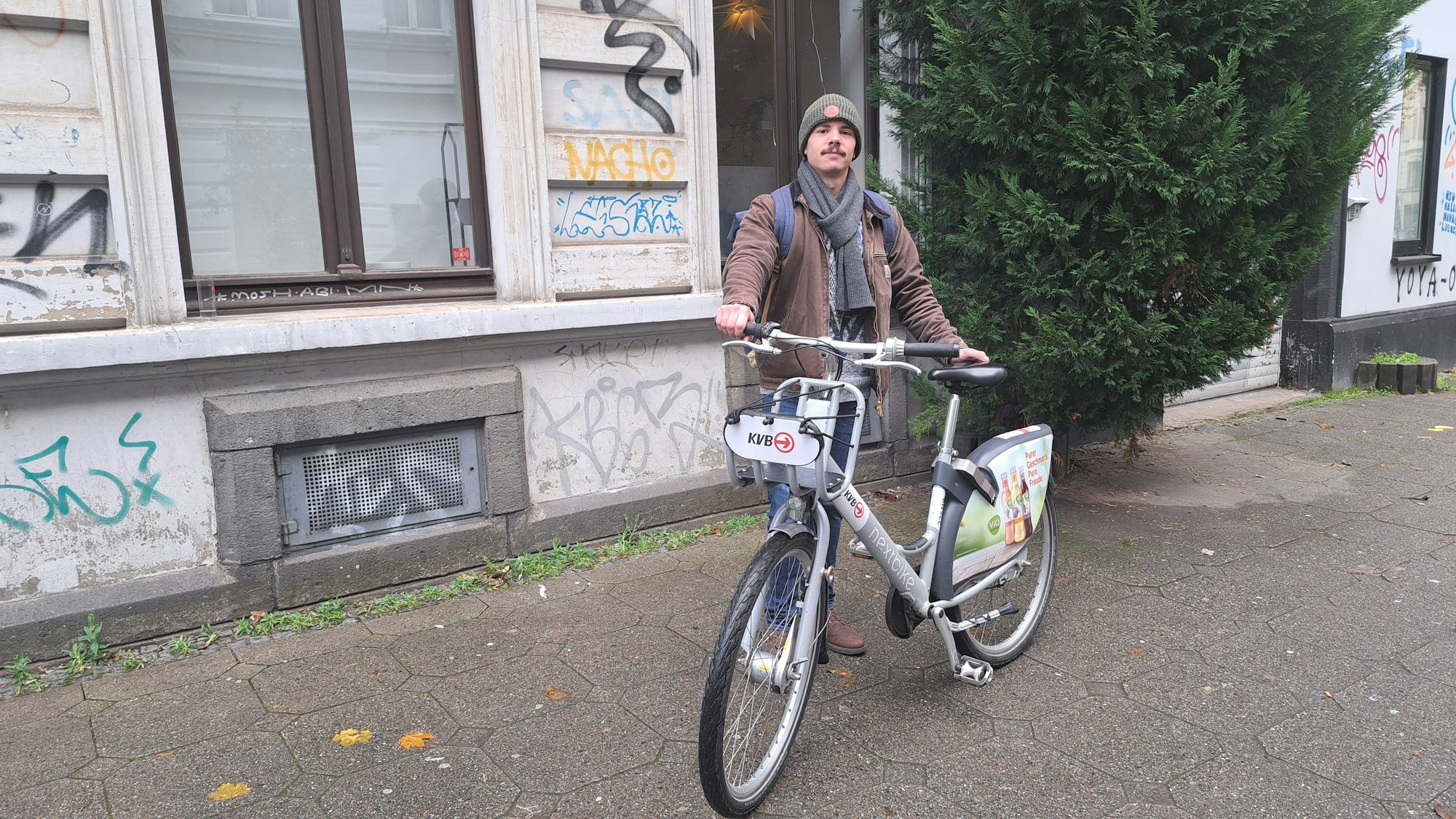 Fabio Botero steht mit einem KVB-Rad auf dem Gehweg.