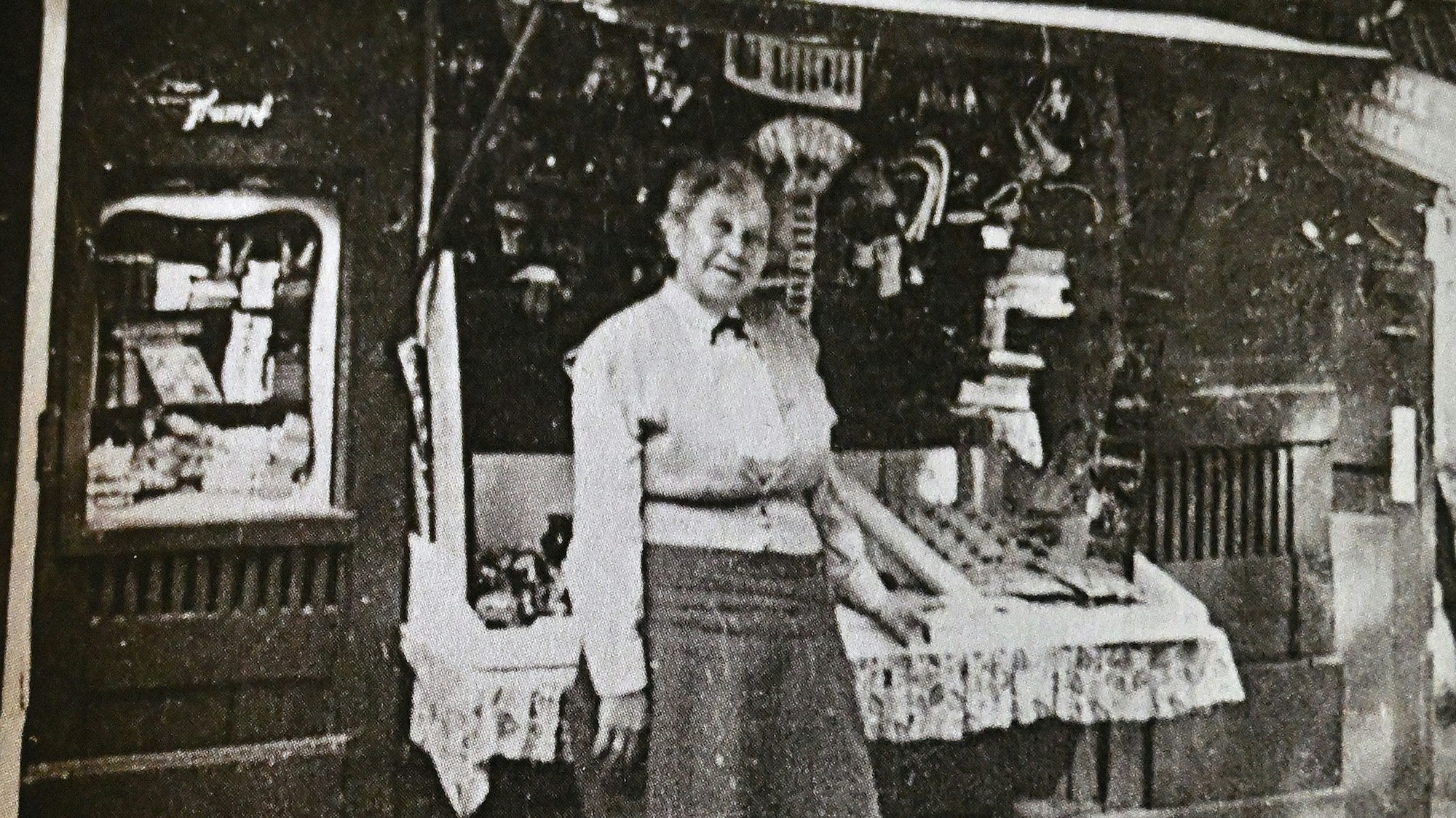 Eine ältere Frau steht vor einem historischen Andenkenbüdchen.