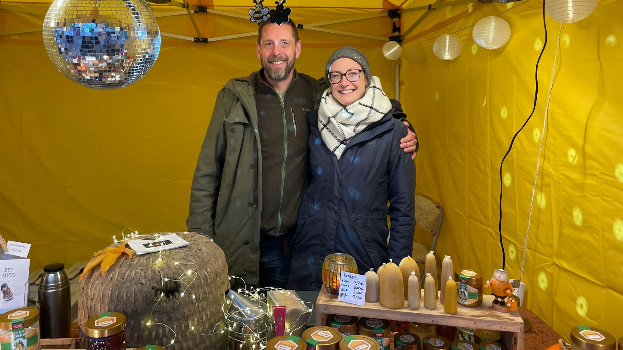 Auf dem Bild ist ein Ehepaar zu sehen, dass an einem Stand Produkte aus seiner Imkerei anbietet.