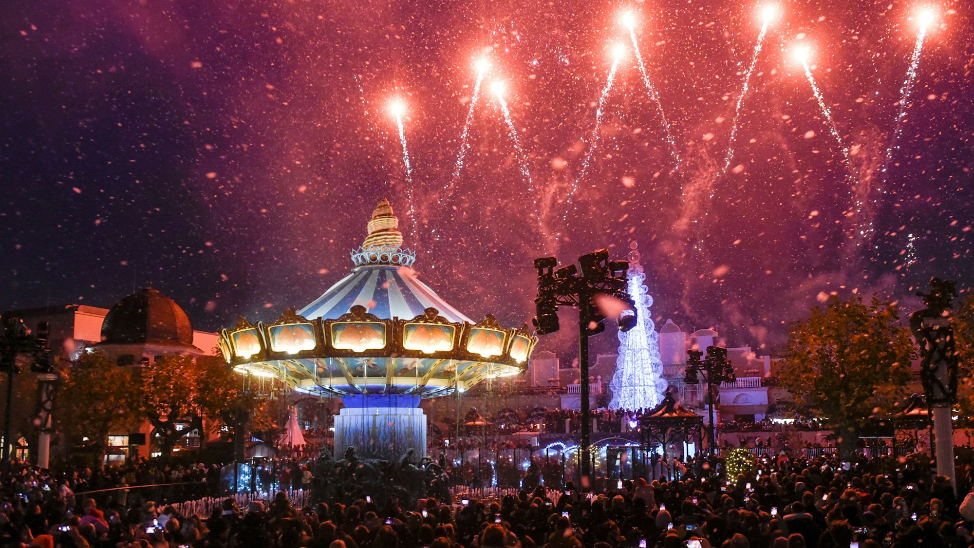 Auf dem Bild sind ein erleuchtetes Karussell und eine Lasershow im Freizeitpark zu sehen.