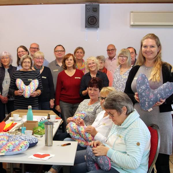 Auf dem Bild ist eine Gruppe von rund 20 Männern und Frauen zu sehen, die Herzkissen für Brustkrebspatienten genäht haben.