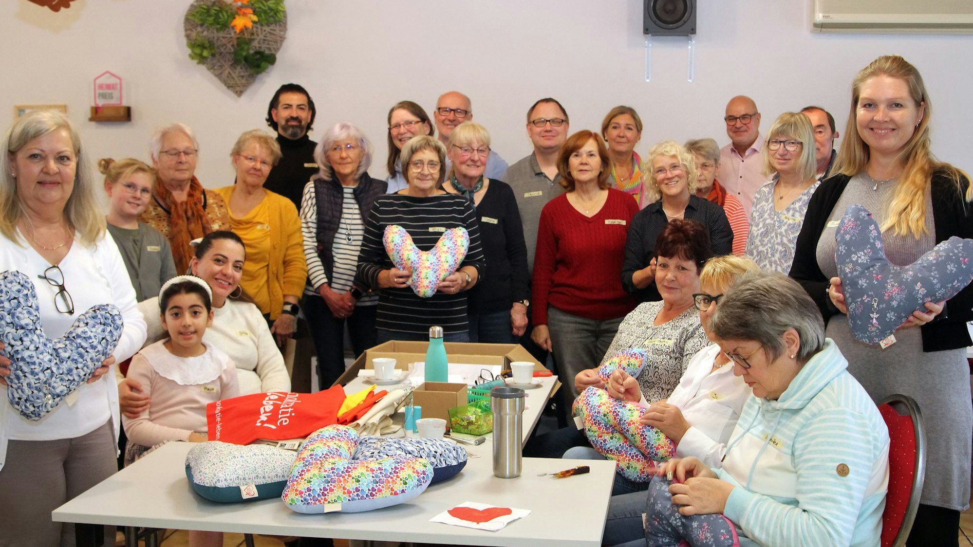 Auf dem Bild ist eine Gruppe von rund 20 Männern und Frauen zu sehen, die Herzkissen für Brustkrebspatienten genäht haben.