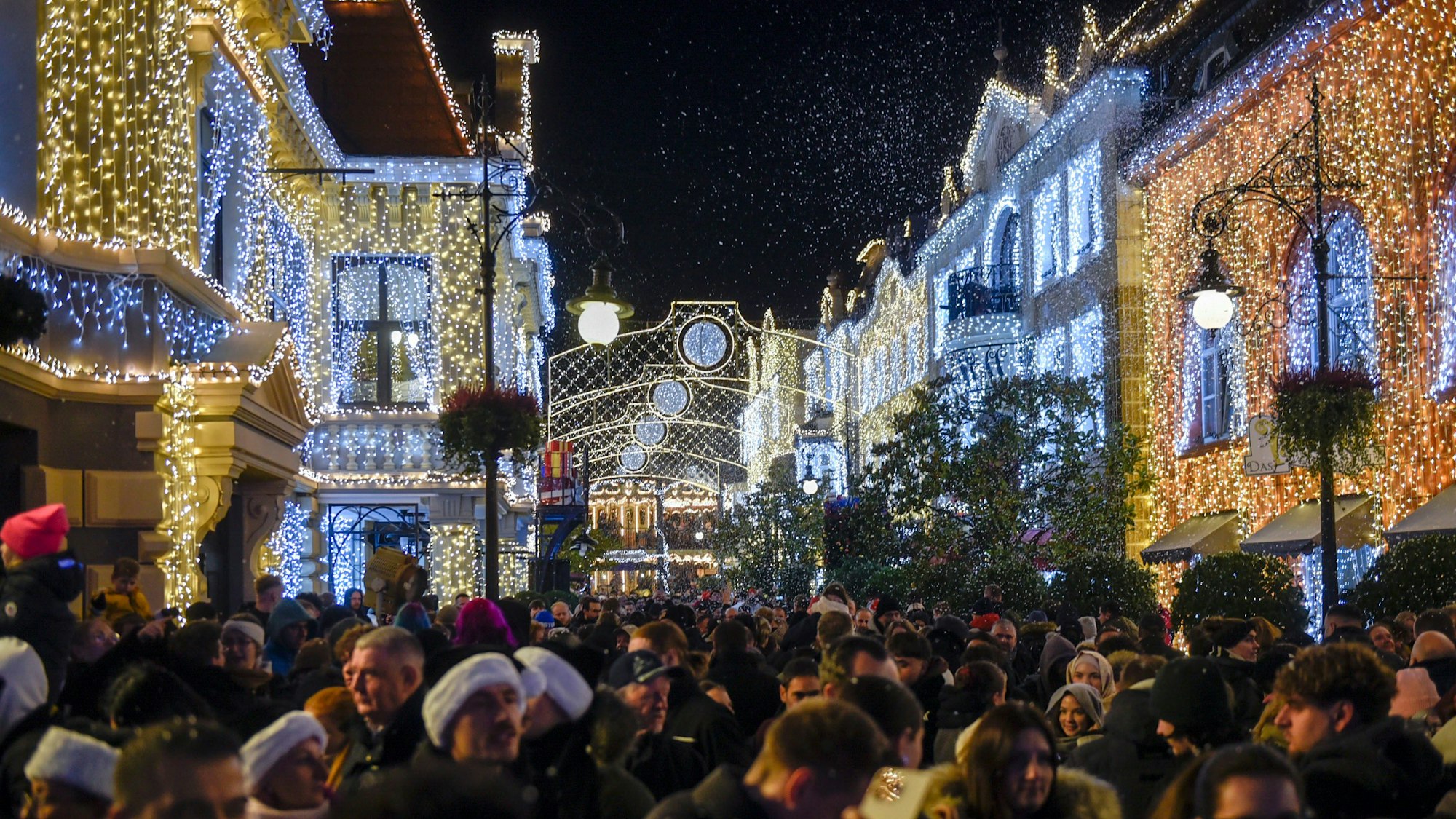 Auf dem Bild sind mit Lichterketten geschmückte Gebäude im Freizeitpark und Besucher zu sehen.