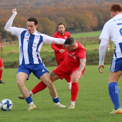 Mit dem Arm hält sich ein Fußballer den Gegenspieler vom Leib, der gleichzeitig von hinten versucht, an den Ball zu gelangen.