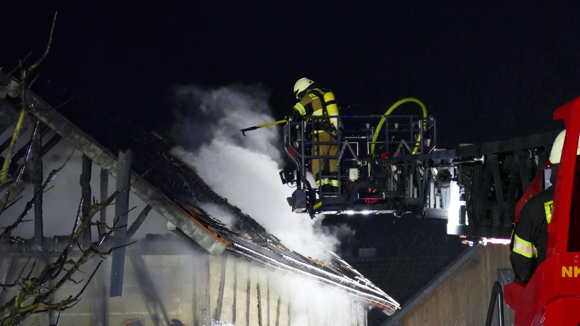Ein Feuerwehrmann im Dreileiterkorb über einem brennenden Gebäude.