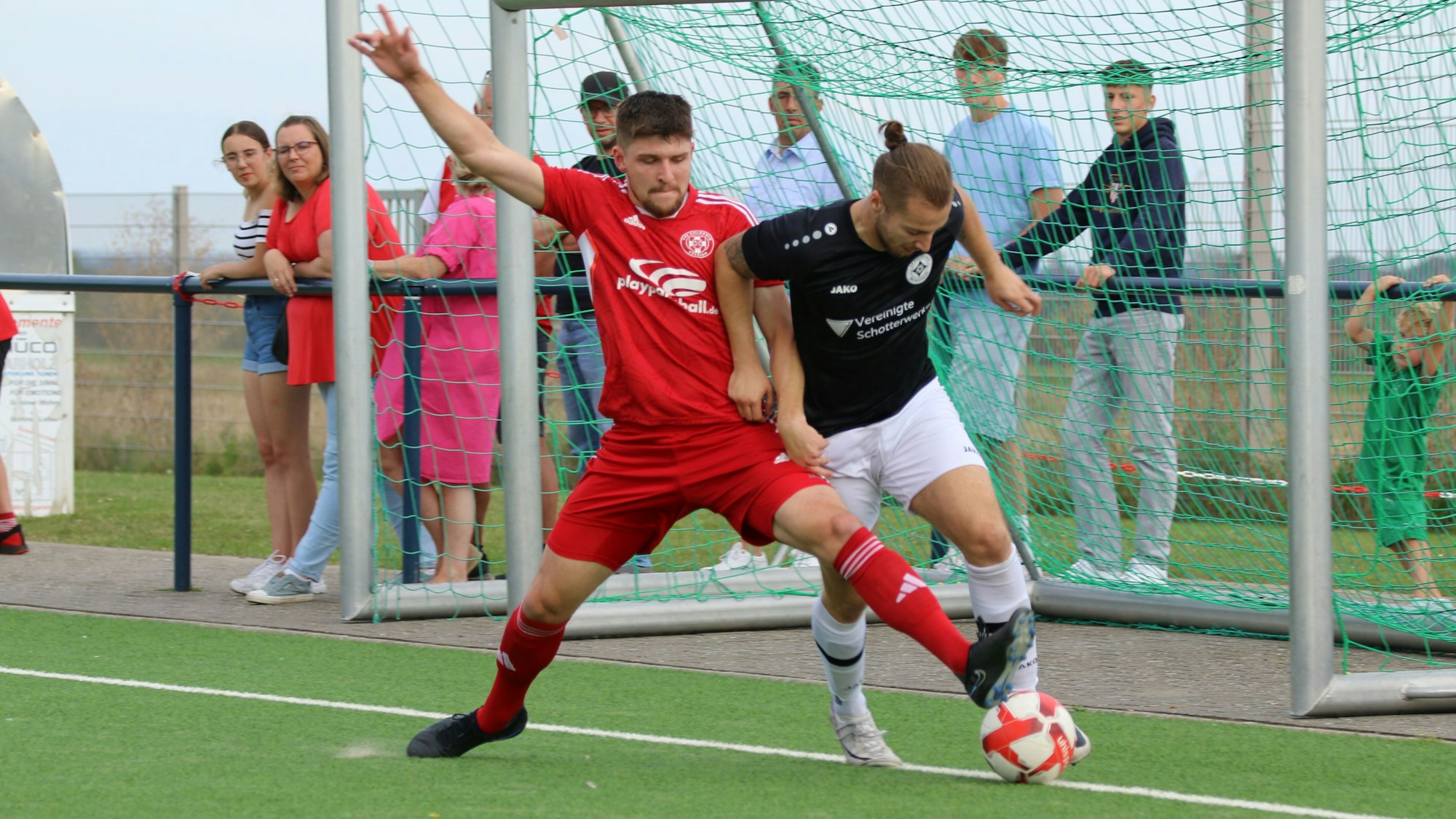 Ein Fußballer erobert mit einem langen Bein an der Außenlinie den Ball von einem Gegenspieler.