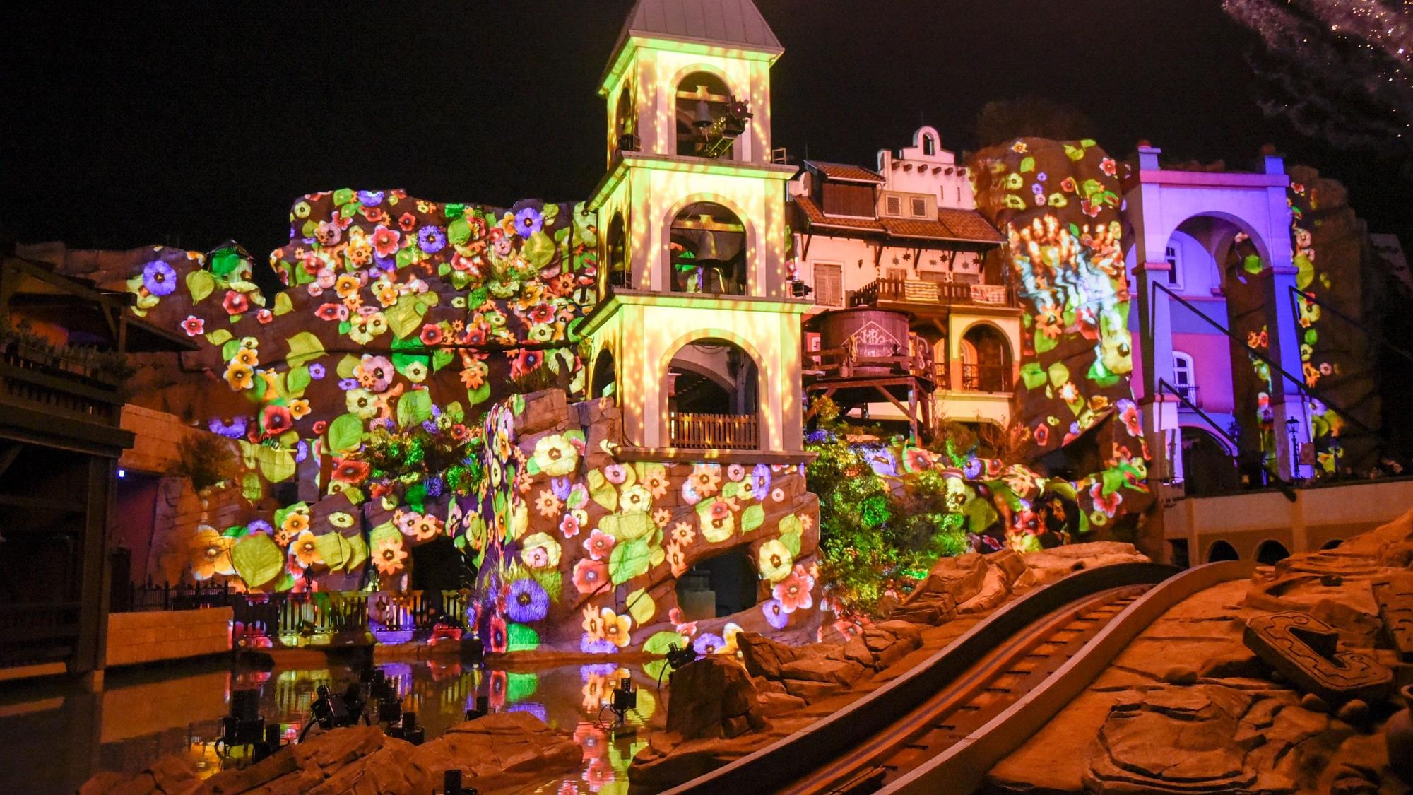 Auf dem Bild ist die Anlage des verbotenen Tempels zu sehen, die mit einer bunten Lichtinstallation mit Blumen angestrahlt wird.