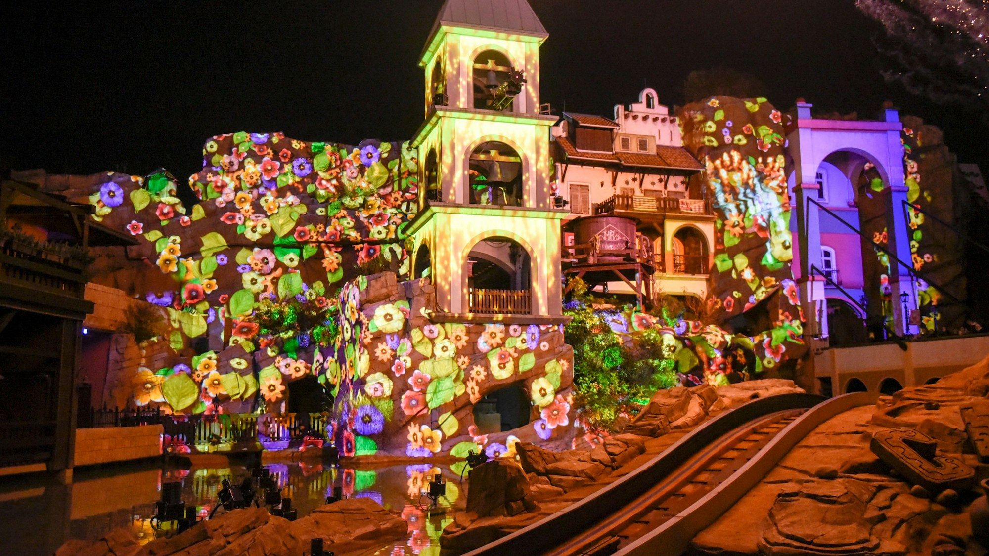 Auf dem Bild ist die Anlage des verbotenen Tempels zu sehen, die mit einer bunten Lichtinstallation mit Blumen angestrahlt wird.
