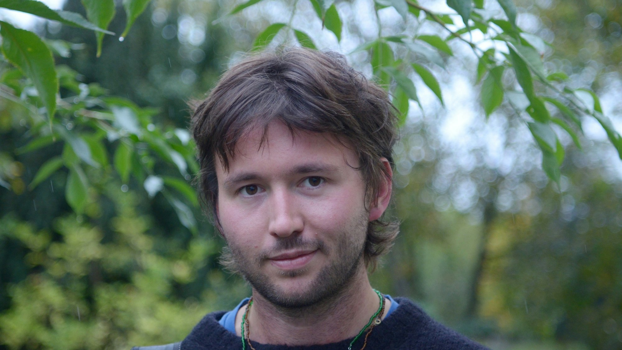 Ein Porträtfoto des Musikers, im Hintergrund Bäume und Sträucher.