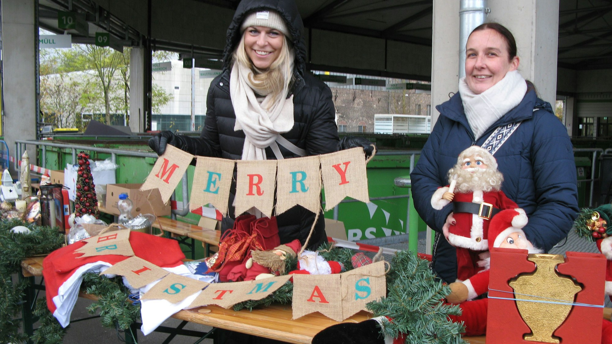 Zwei Frauen stehen hinter einem Tisch mit weihnachtlichen Dekorationsartikeln.