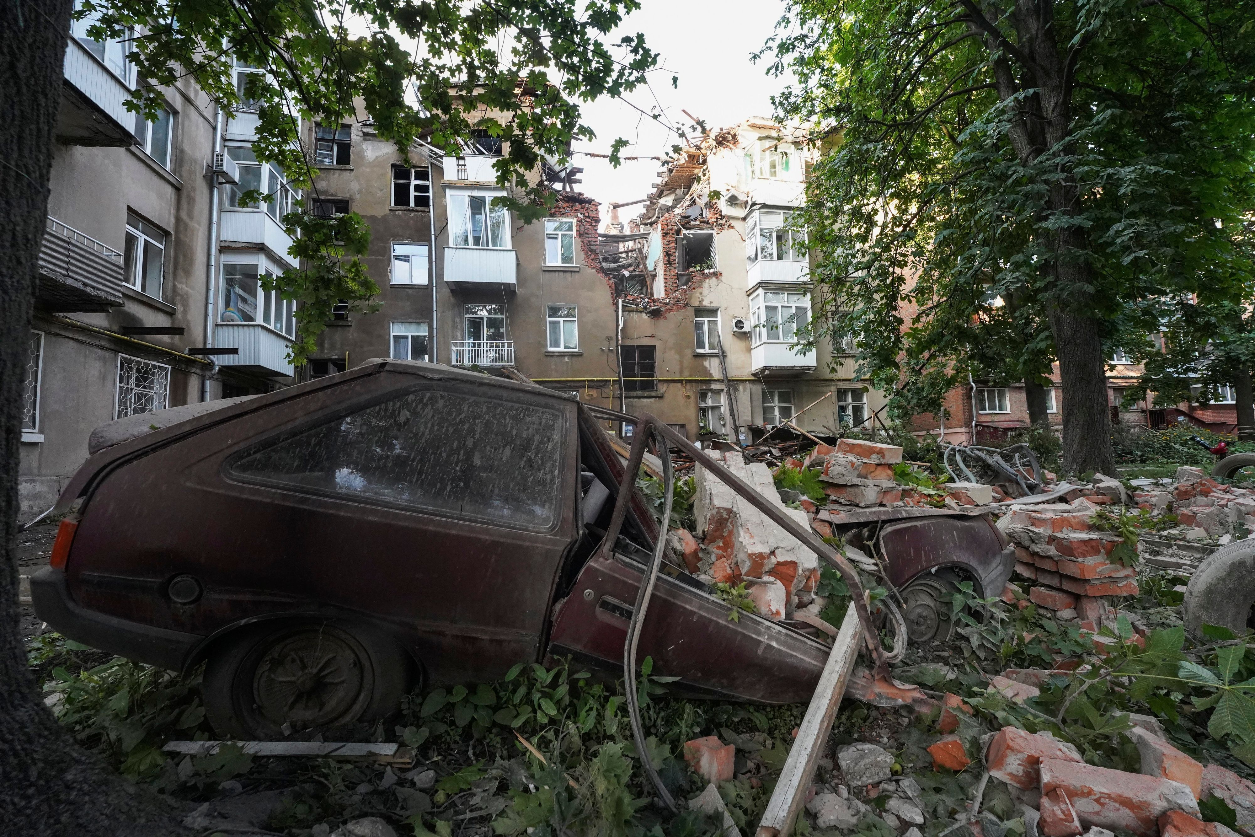 Ein Autowrack ist nach einem Angriff vor einem beschädigten Wohnhaus zu sehen.