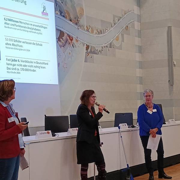 Zu sehen sind drei Frauen vor einer Beamer-Präsentation.