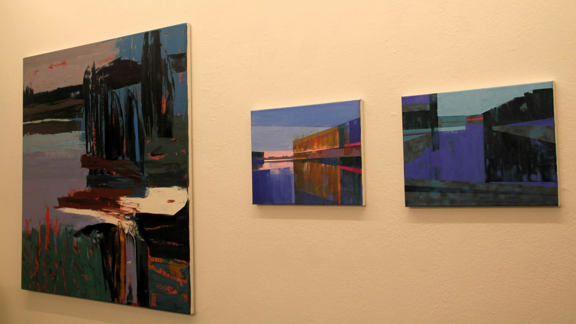 An einer Wand hängen drei Gemälde nebeneinander.