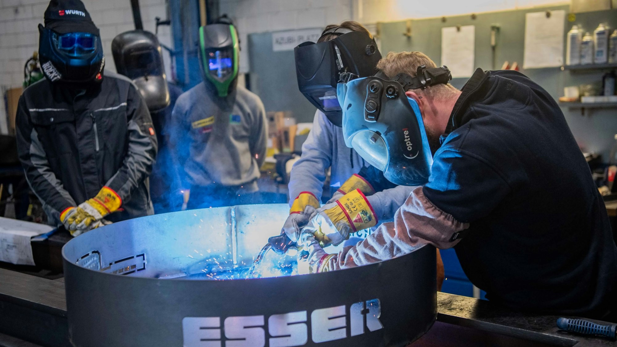 Schüler der Realschule Bad Münstereifel stehen mit Schutzmasken an einer Ascheschale und schweißen. Ihre Gesichter sind in blaues Licht getaucht und es fliegen Funken.