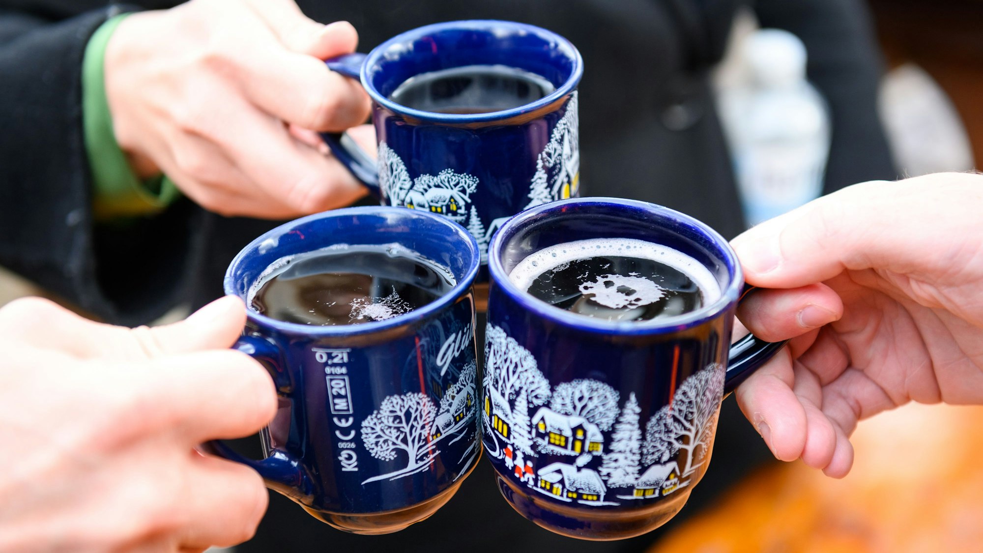 Drei Glühweinbecher werden angestoßen.