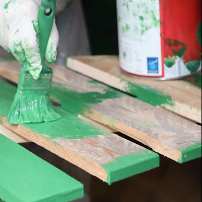 Auf dem Bild sind ein Pinsel mit grüner Farbe und Holzlatten zu sehen.