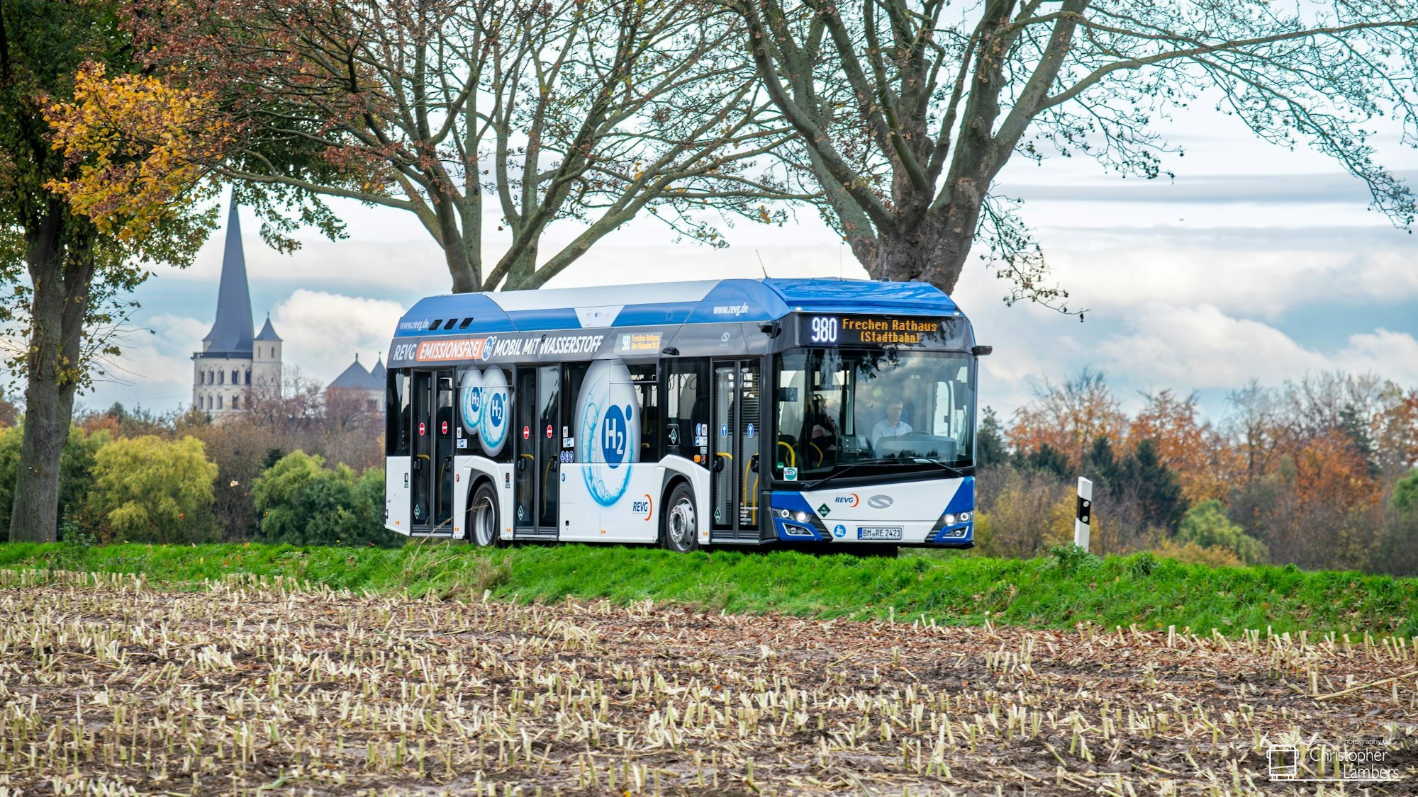 Auf dem Foto ist ein blau-weißer Bus zu sehen, der eine Landstraße befährt.
