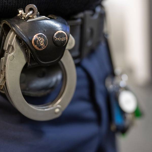 Eine Handschelle hängt am Gürtel eines Polizisten