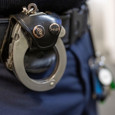 Eine Handschelle hängt am Gürtel eines Polizisten