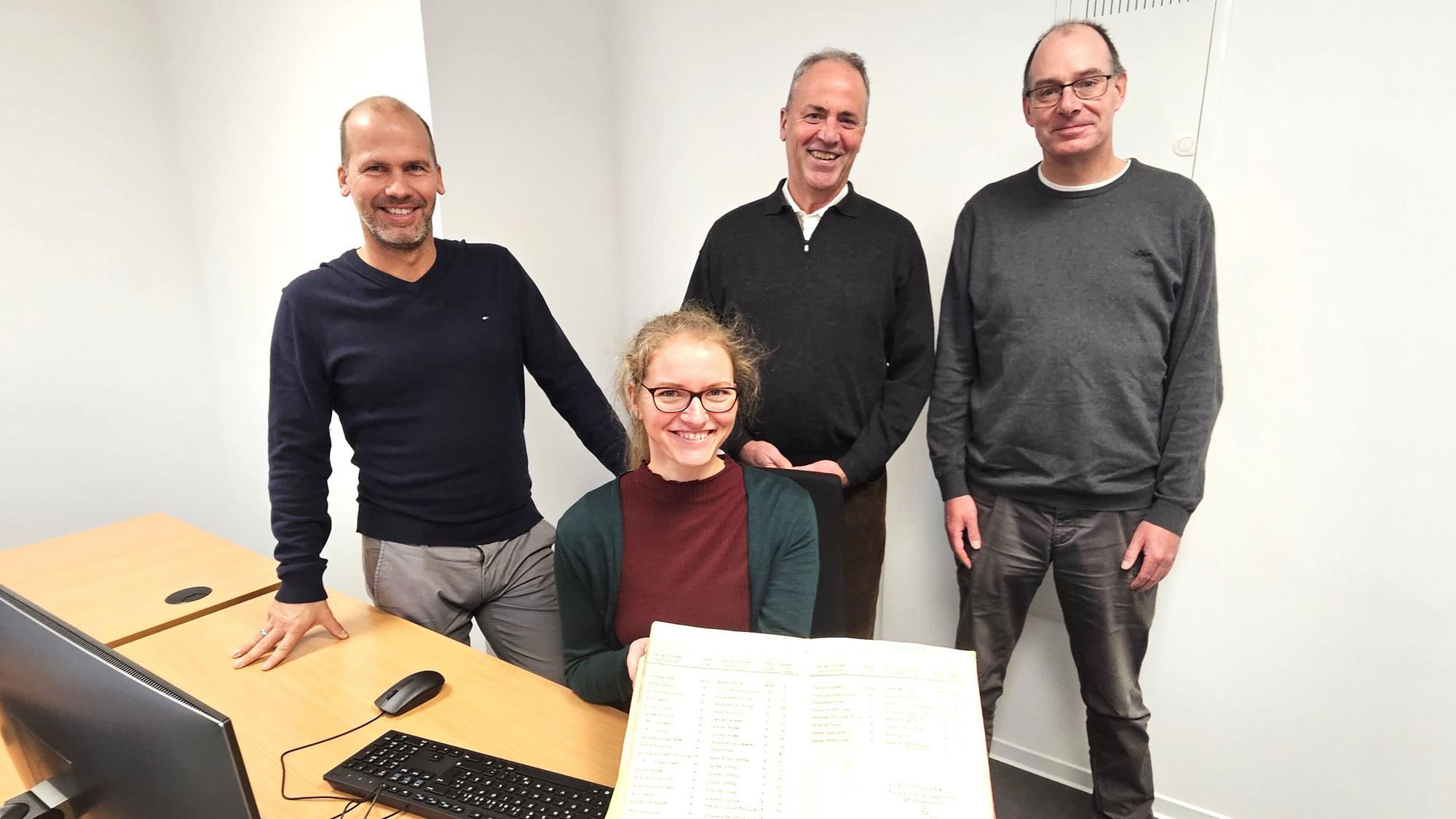 Markus Auel, Hermann-Josef Esser und Lothar Schatten stehen hinter der sitzenden Nicole Gutmann, die ein Familienbuch präsentiert.