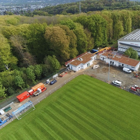 Blick aus der Vogelperspektive auf einen Fußballplatz, neue Umkleidegebäude und eine große Sporthalle.