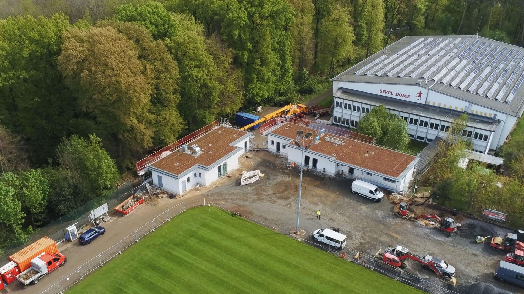 Blick aus der Vogelperspektive auf einen Fußballplatz, neue Umkleidegebäude und eine große Sporthalle.
