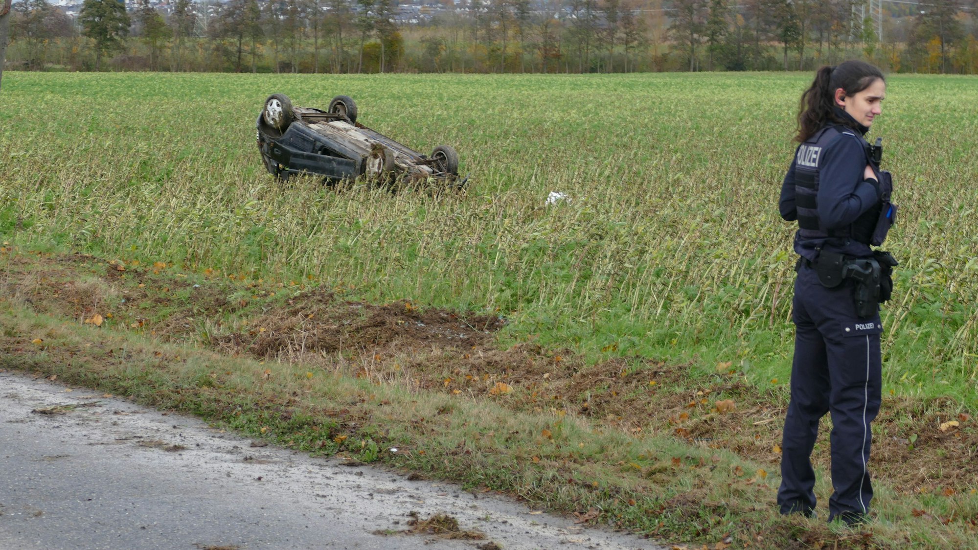 Eine Polizistin steht am Straßenrand, im Feld liegt das verunglückte Auto.