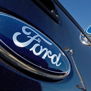 Ein Ford-Logo auf der Heckklappe eines Pick-up-Trucks ist vor dem Schild eines Ford-Händlers zu sehen.