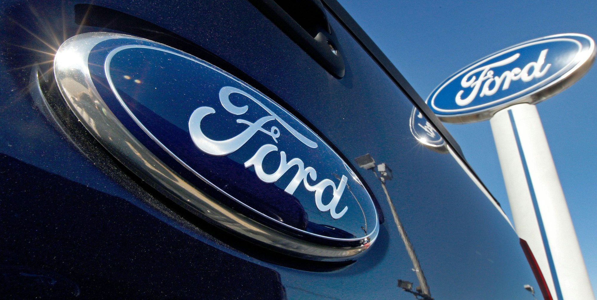Ein Ford-Logo auf der Heckklappe eines Pick-up-Trucks ist vor dem Schild eines Ford-Händlers zu sehen.