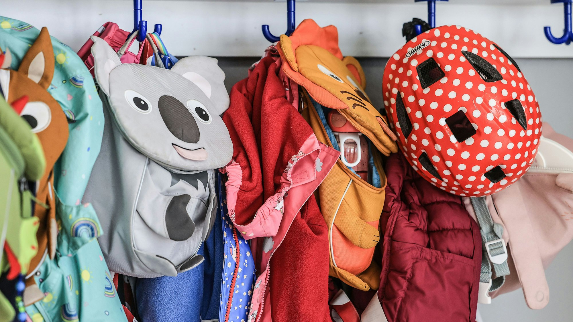 Kleidung und Taschen von Kindern hängen im Flur einer Kindertagesstätte.