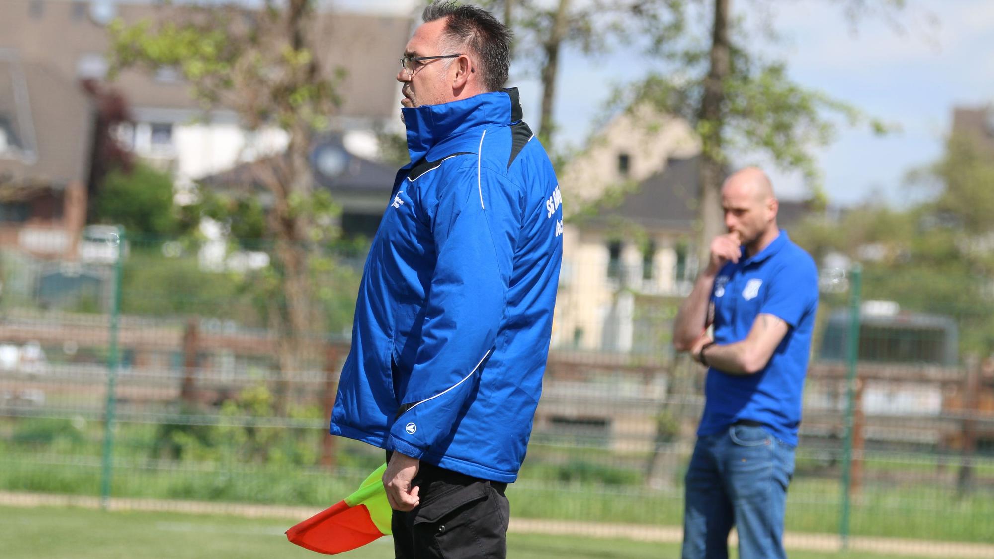 Zwei Trainer beobachten ein Fußballspiel. Einer von ihnen hält die Assistentenfahne in der Hand.