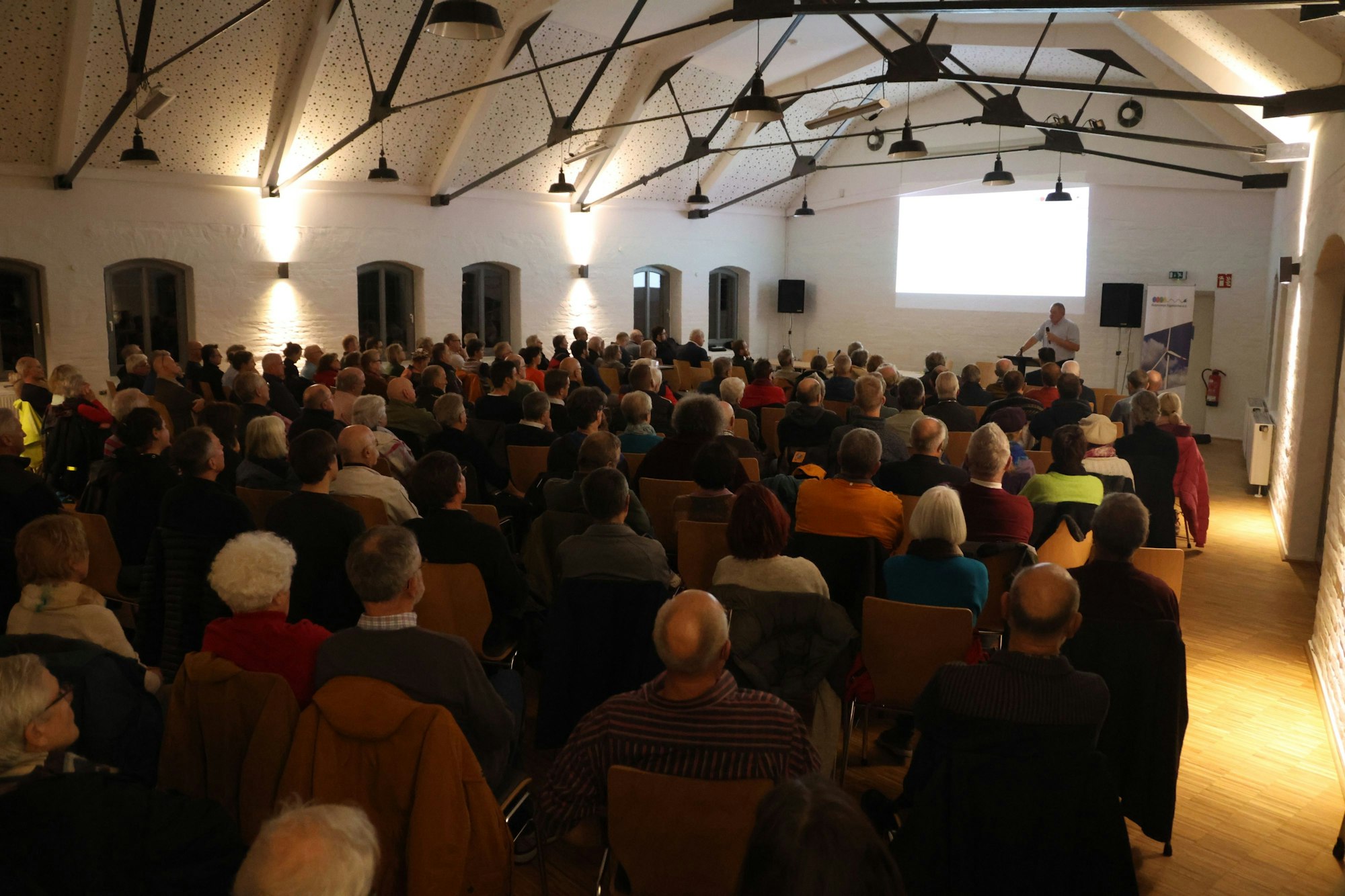 Eine Grippe Menschen sitzt in einem großen Saal und schaut in Richtung Bühne.