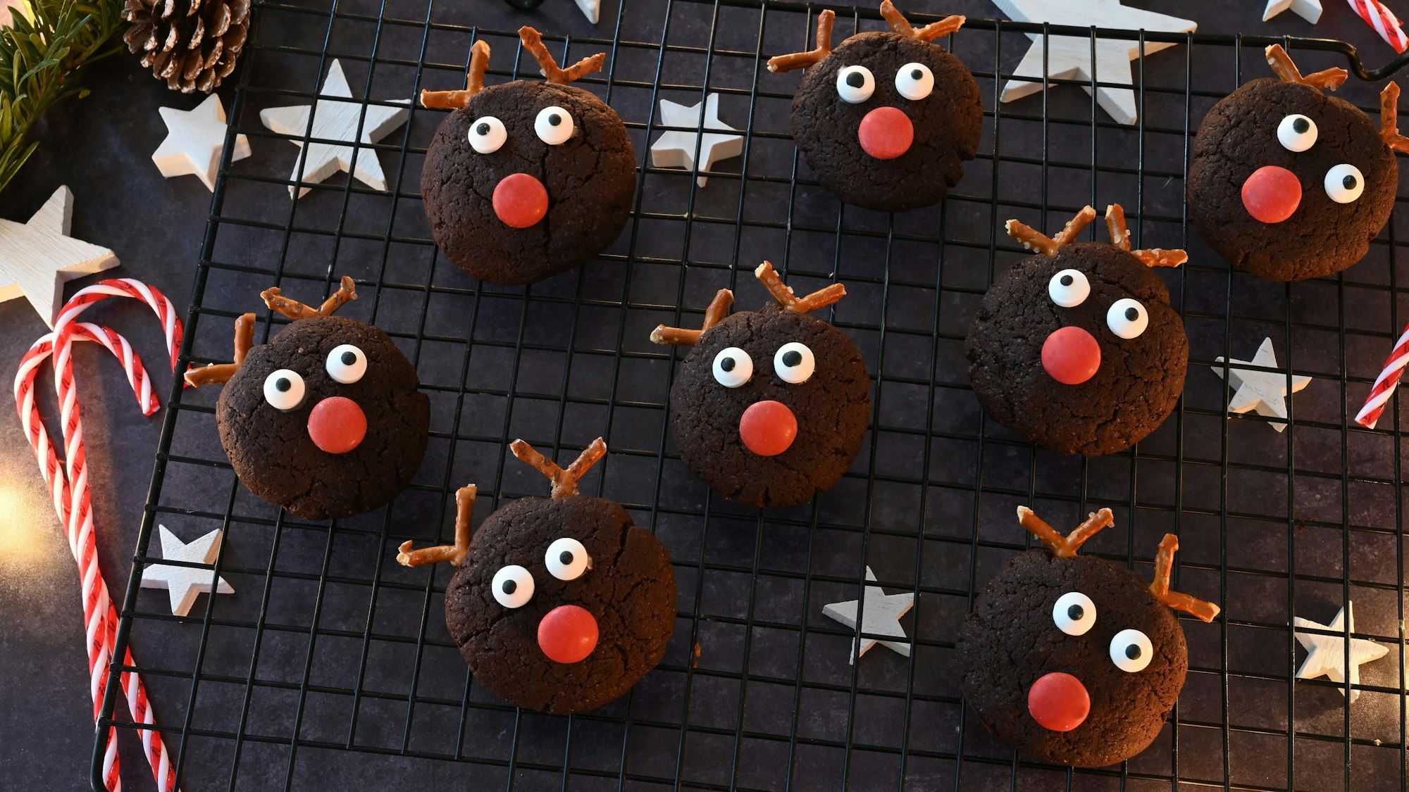 Kekse mit Augen, einer roten Schokolinse und Brezelgeweih liegen auf einem Gitter.