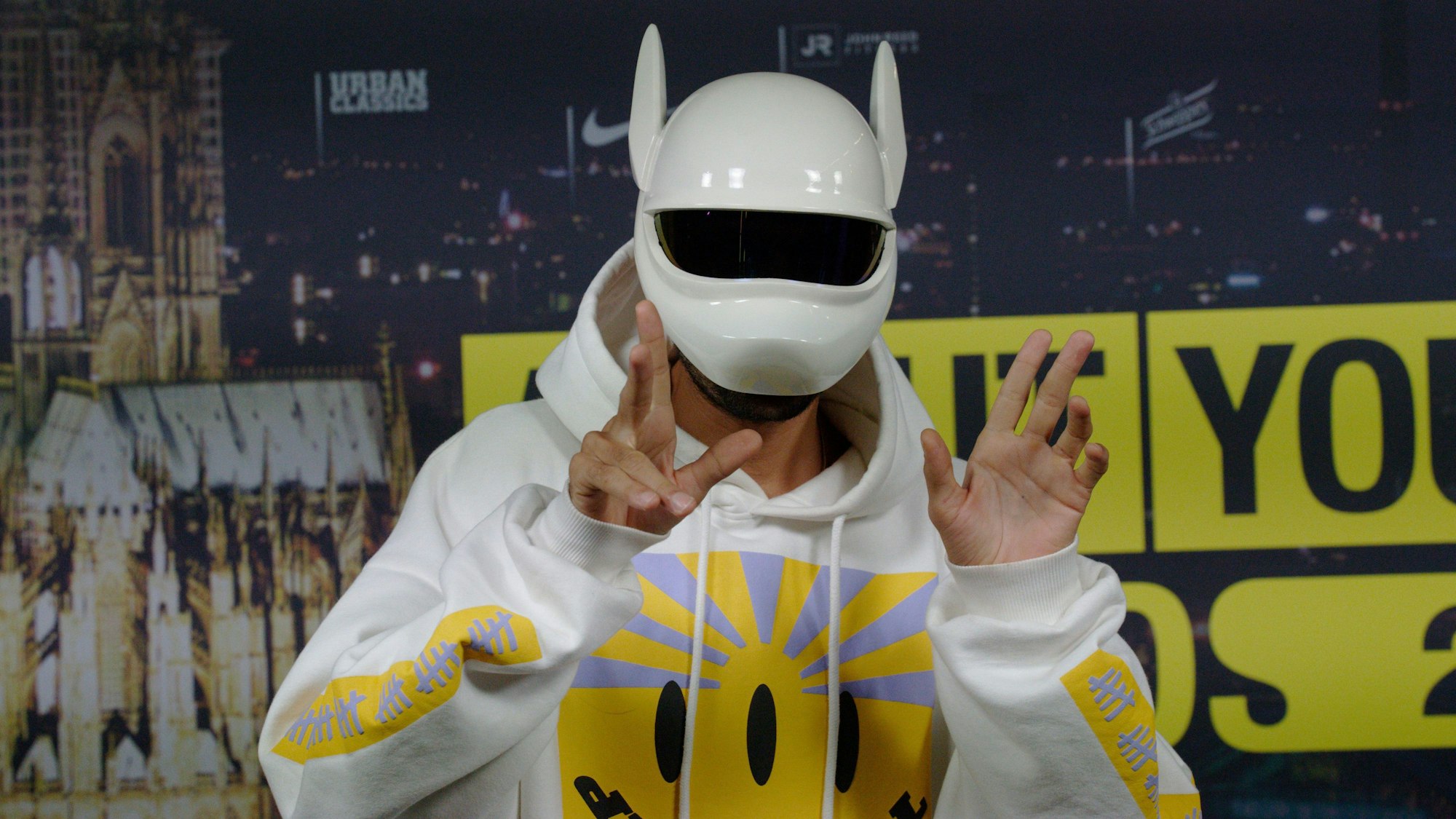 Cro steht mit seiner Maske vor einer Leinwand.