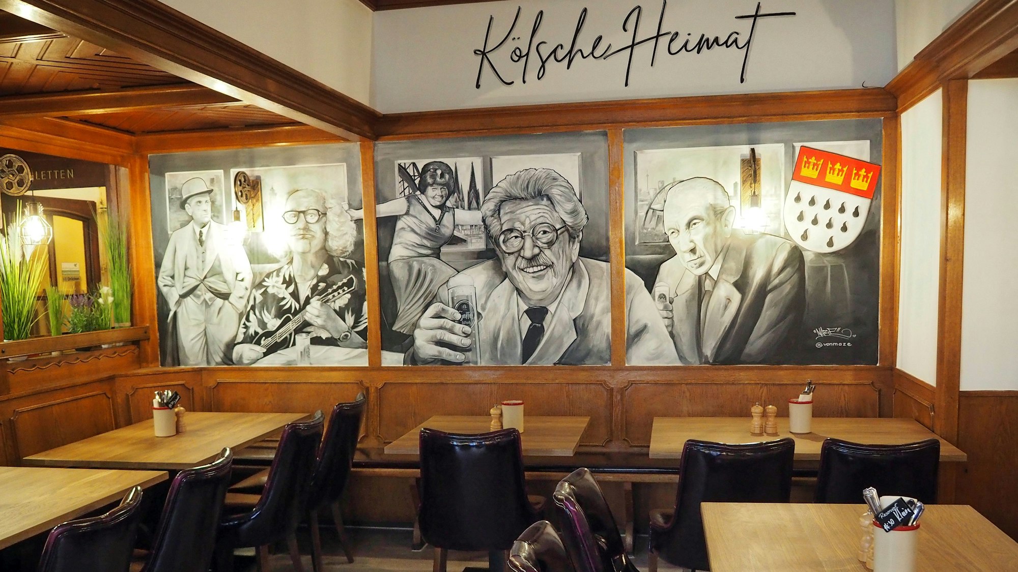 Den hinteren Speiseraum der „Kölsche Heimat“ schmückt ein schwarz-weißes Wandbild, auf dem Millowitsch, Adenauer und weitere Promis zu sehen sind.