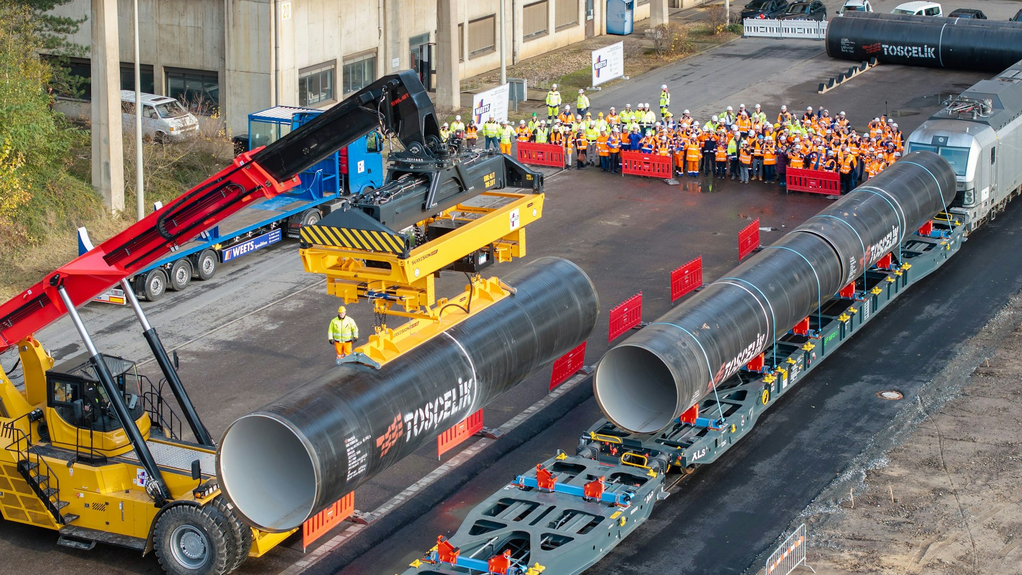 Ein Fahrzeug hebt ein riesiges Rohr von einem Güterzug.