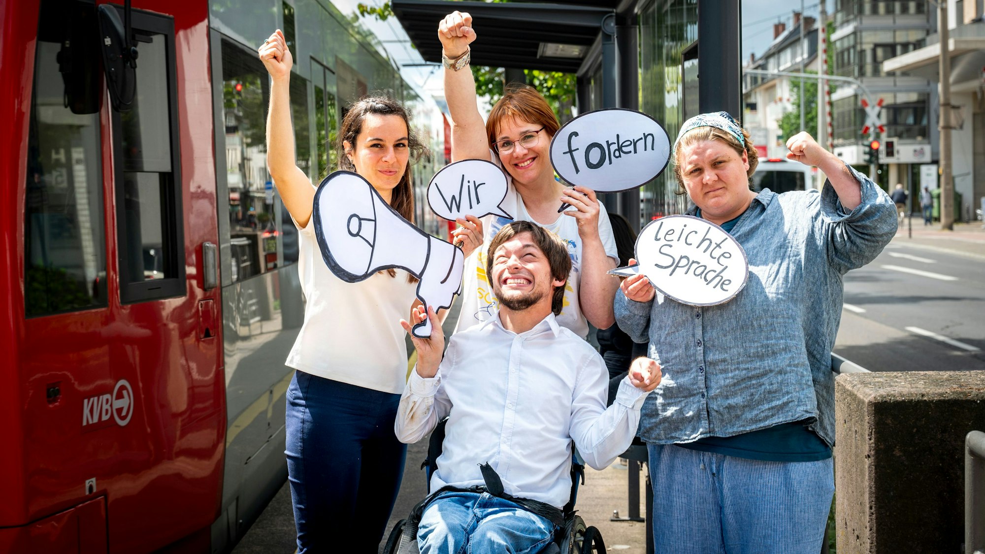 Auf dem Bild stehen Margarita Lüdtke Miró (v. l). Maximilian Westphal (vorne), Silke Degwitz und Dinah Köppen an einer KVB-Haltestelle. Sie halten Protestplakate.