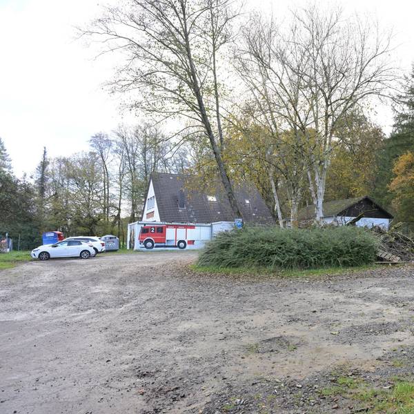 Ein Schotterparkplatz, dahinter ein Feuerwehrhaus.