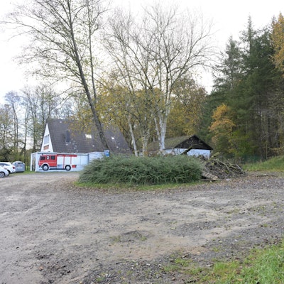 Ein Schotterparkplatz, dahinter ein Feuerwehrhaus.