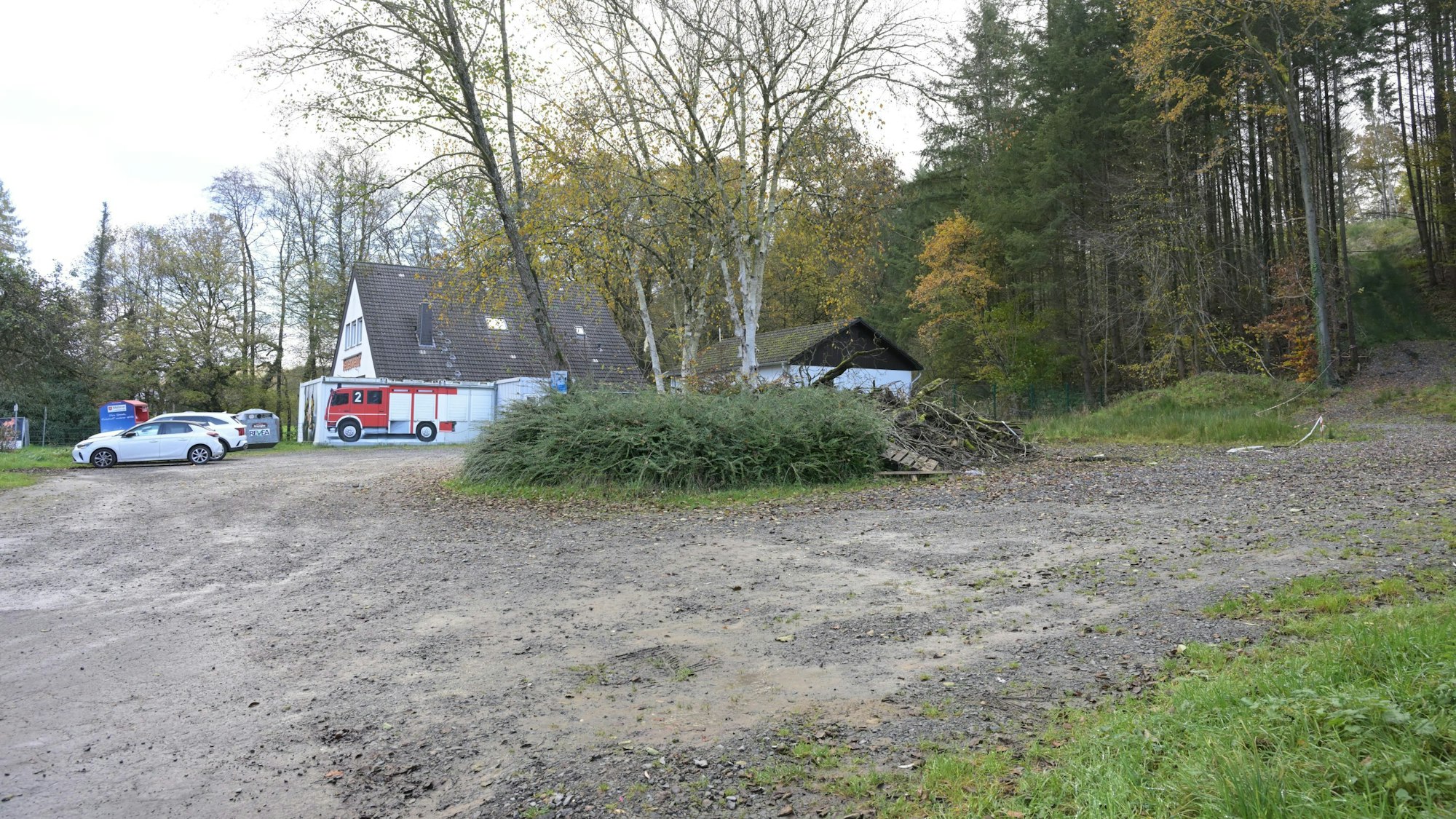 Ein Feuerwehrgerätehaus, daneben ein großer, unbefestigter Parkplatz.