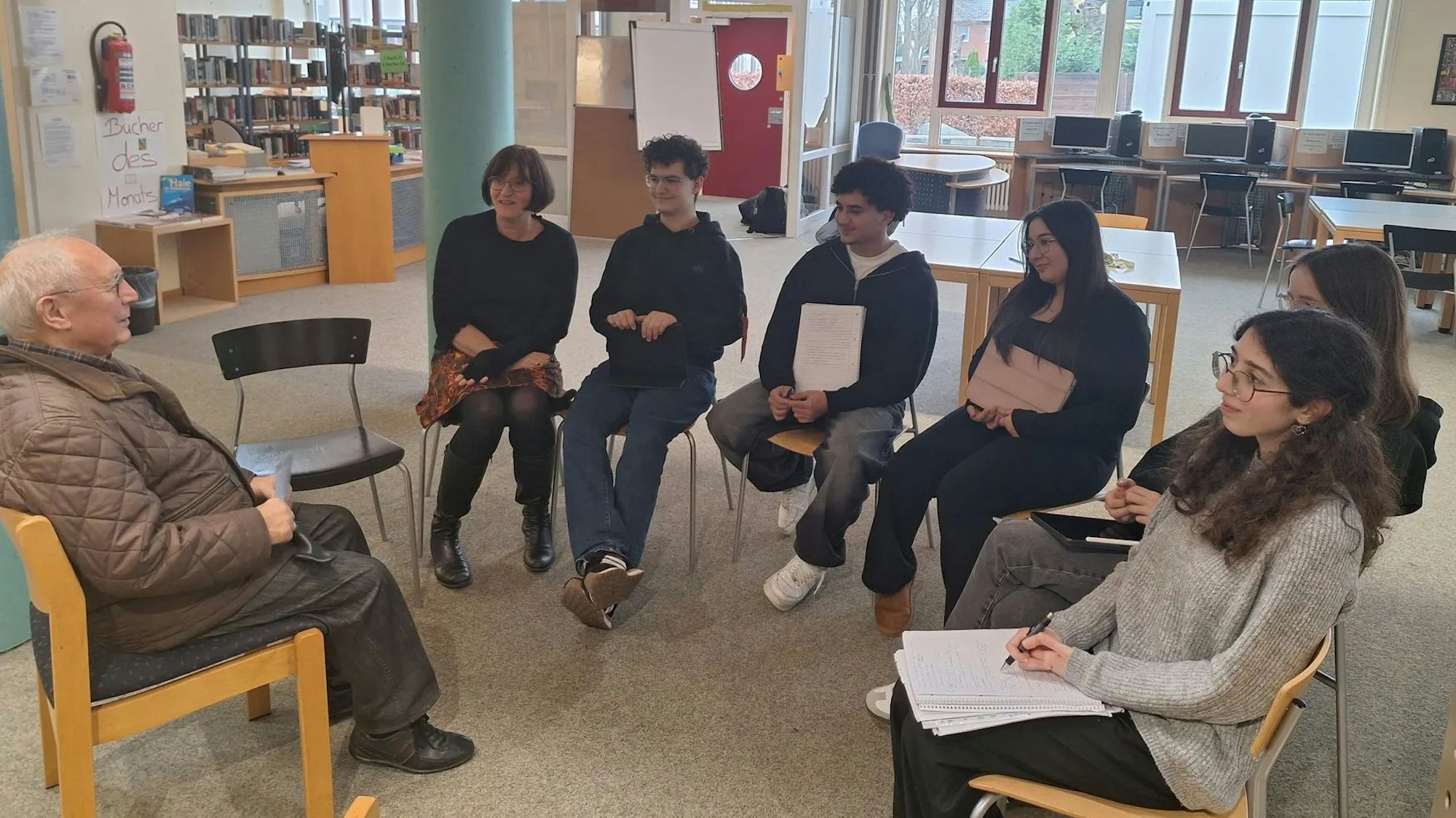 Gino Fidanza sitzt in der Bibliothek der Gesamtschule mit einigen Schülerinnen und Schülern in einem Stuhlkreis.