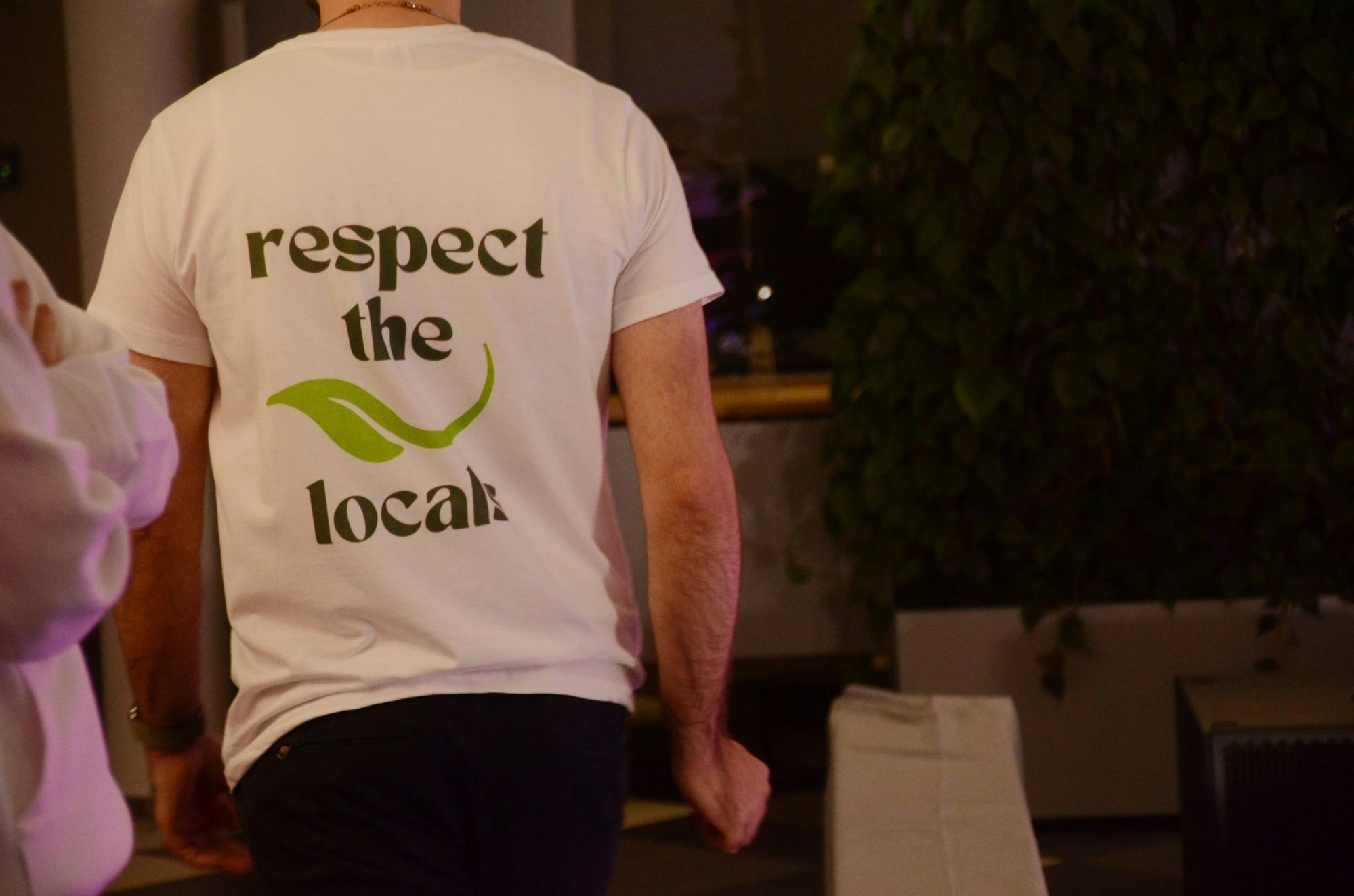 Ein Mann trägt ein weißes T-Shirt, auf dem Rücken steht der Schriftzug "Respect the locals".