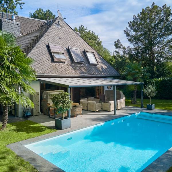 Eine Villa mit schwarzem Dach, davor eine Terrasse und ein Pool.