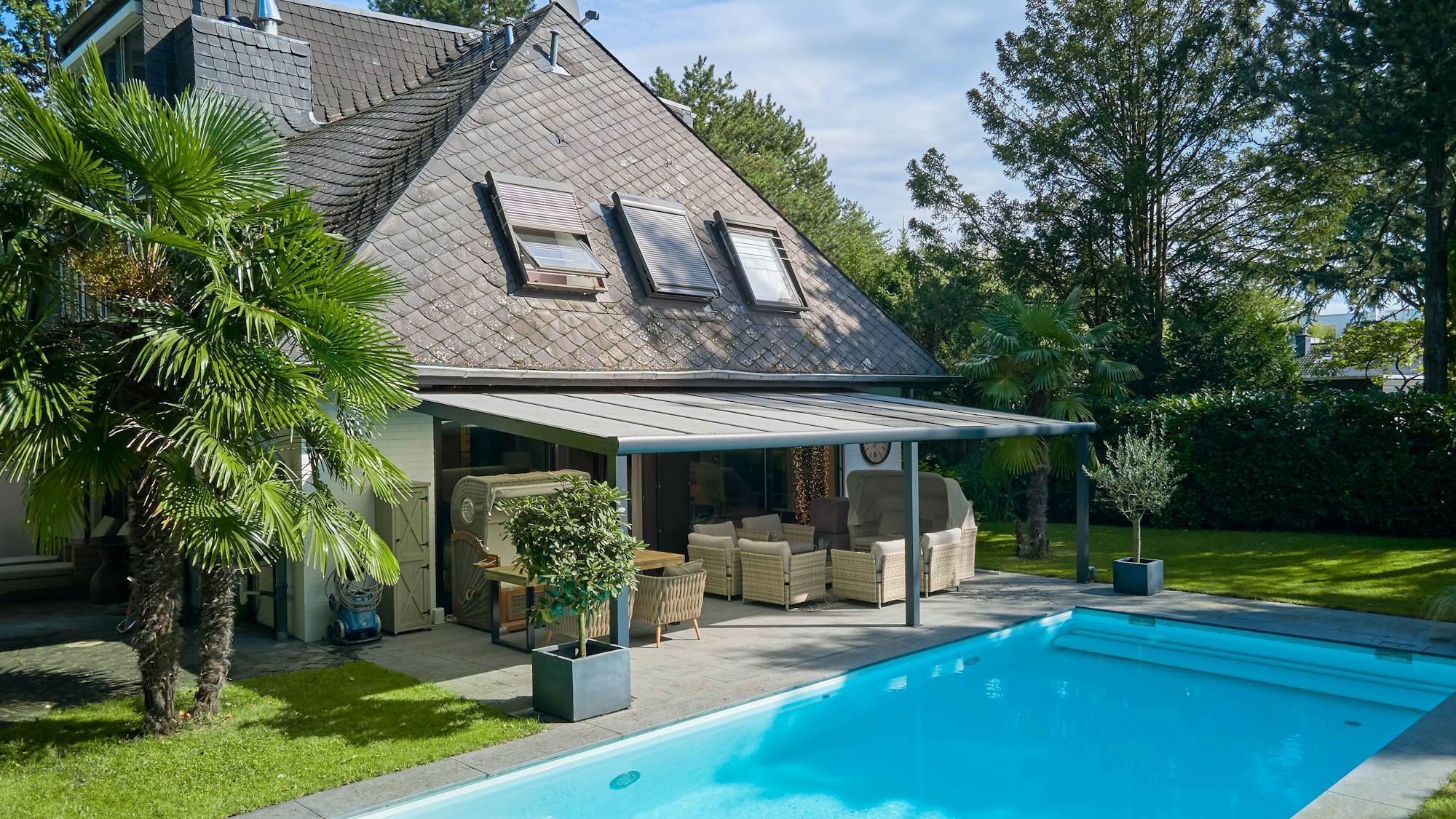 Eine Villa mit schwarzem Dach, davor eine Terrasse und ein Pool.