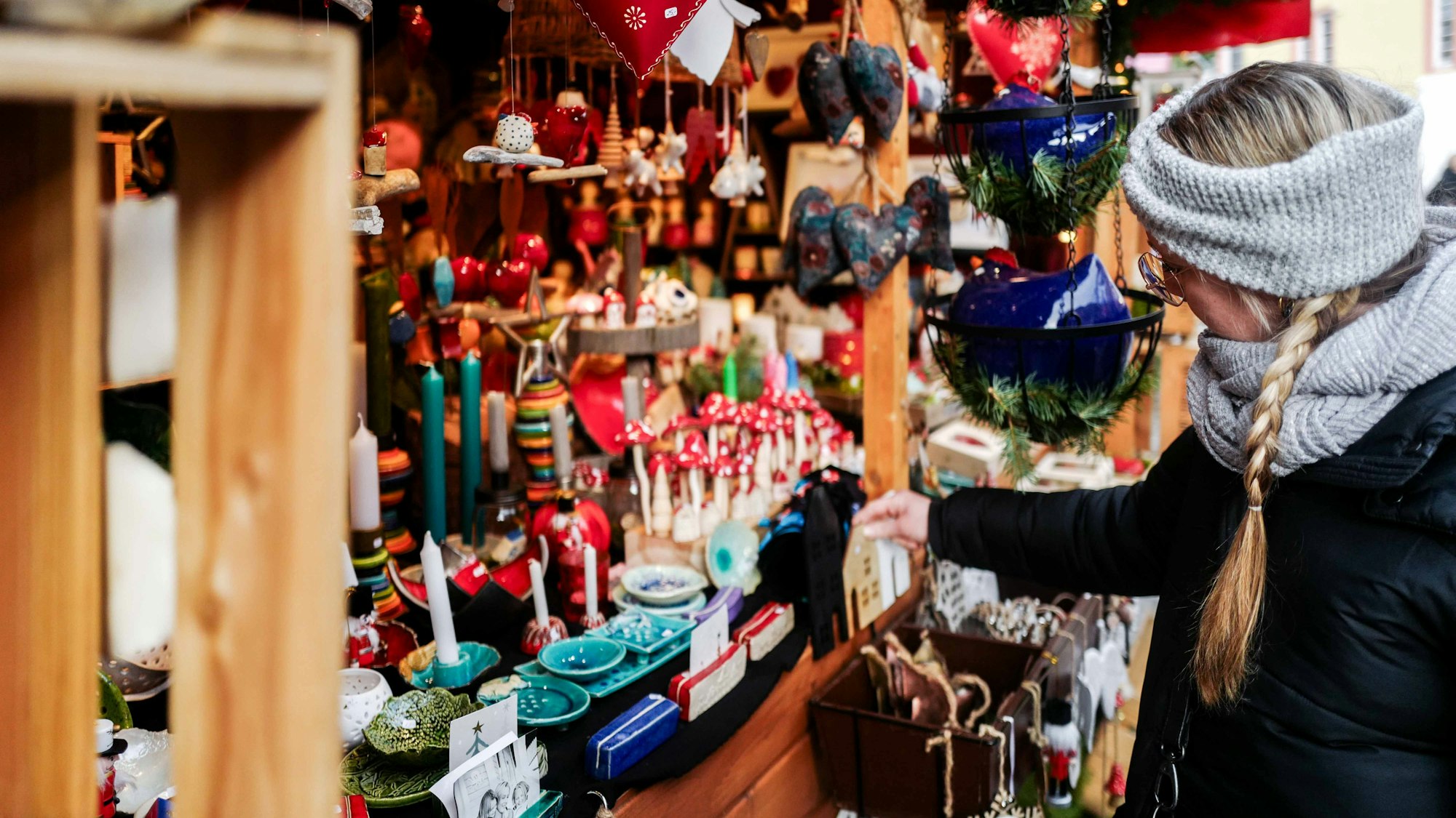 Das Bild zeigt eine Frau, die sich Deko an einer Weihnachtsbude anschaut.