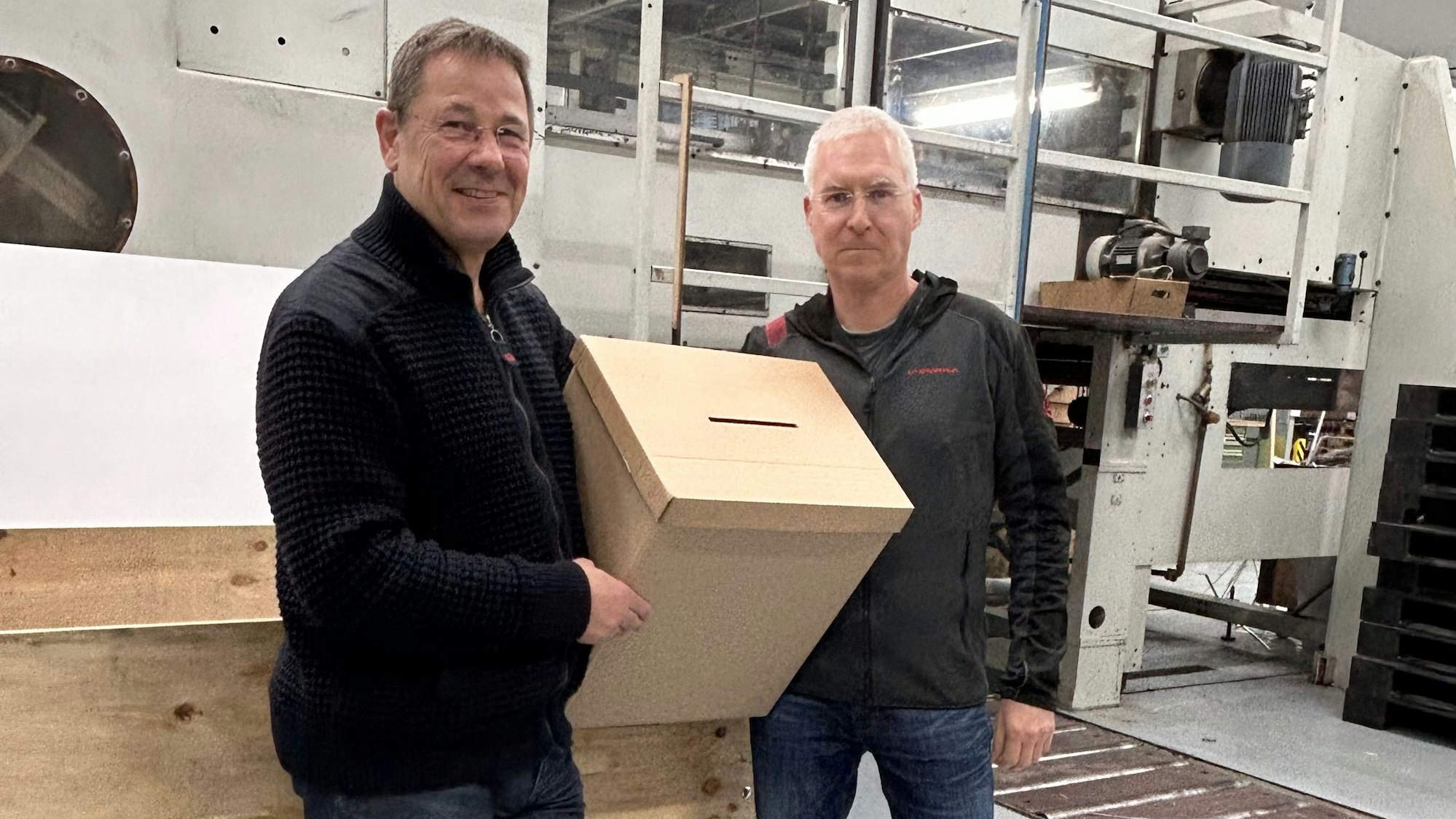 Die beiden Geschäftsführer halten eine Kartonage ins Bild - als Beweis dafür, dass sie Wahlurnen herstellen könnten.