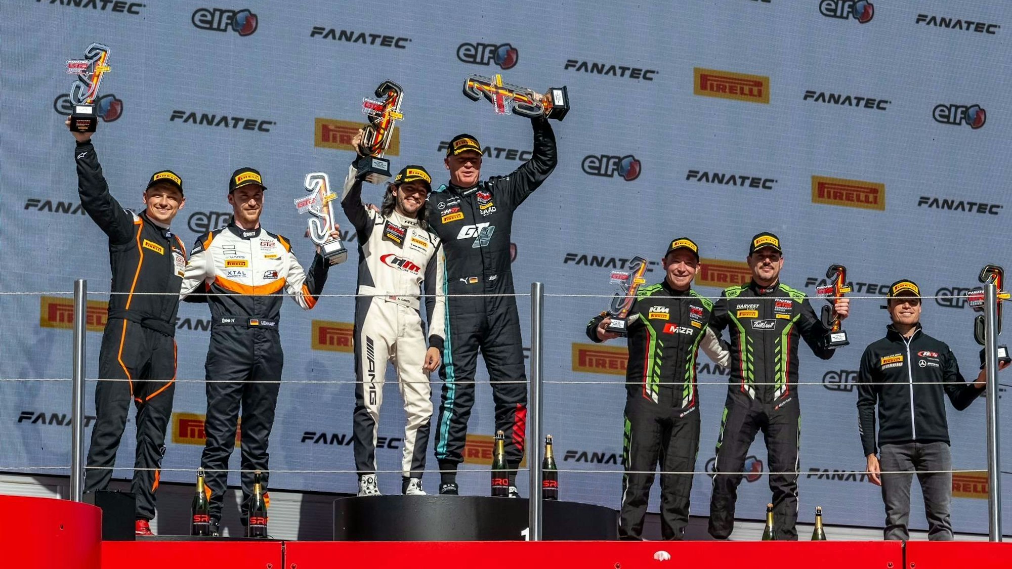 Rennfahrer Jörg Viebahn steht mit einem Teamkollegen auf einem Podest und hält einen Pokal in die Höhe.